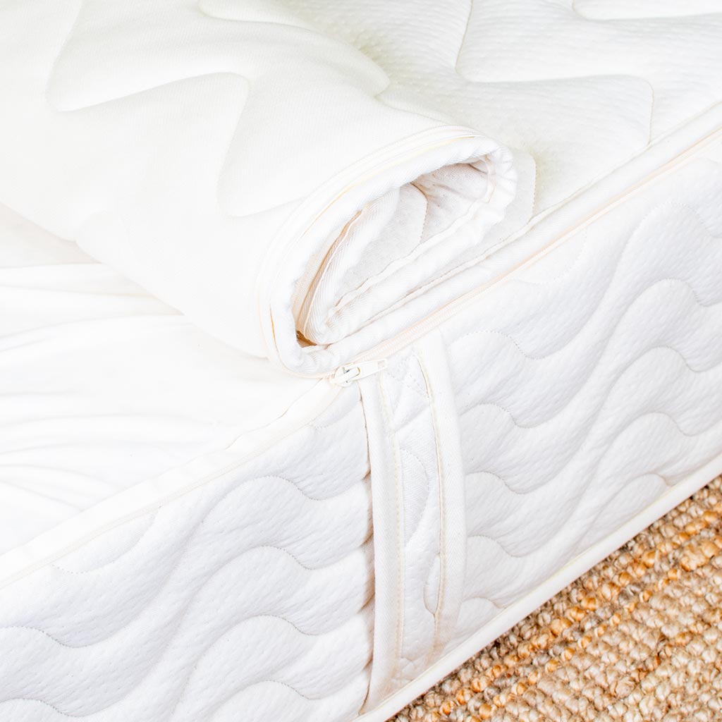 Close-up of a white quilted mattress pad on a bed with a textured beige carpet.