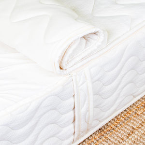 Close-up of a white quilted mattress pad on a bed with a textured beige carpet.